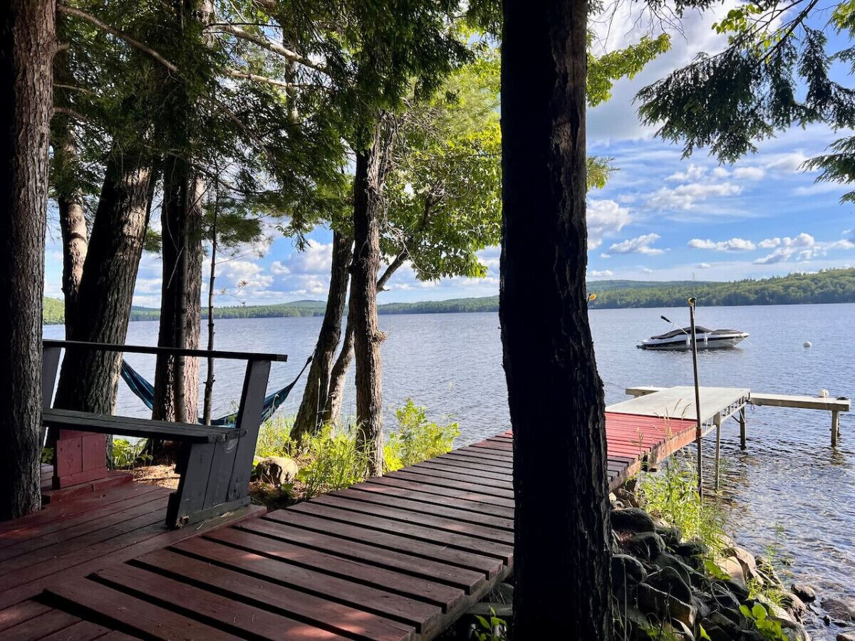 A wooden dock extending into a lake, surrounded by trees, with a boat docked at the end.