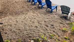 A lakeside setting with blue chairs lined up along the shore, a small dock, and a person sitting on the sand.