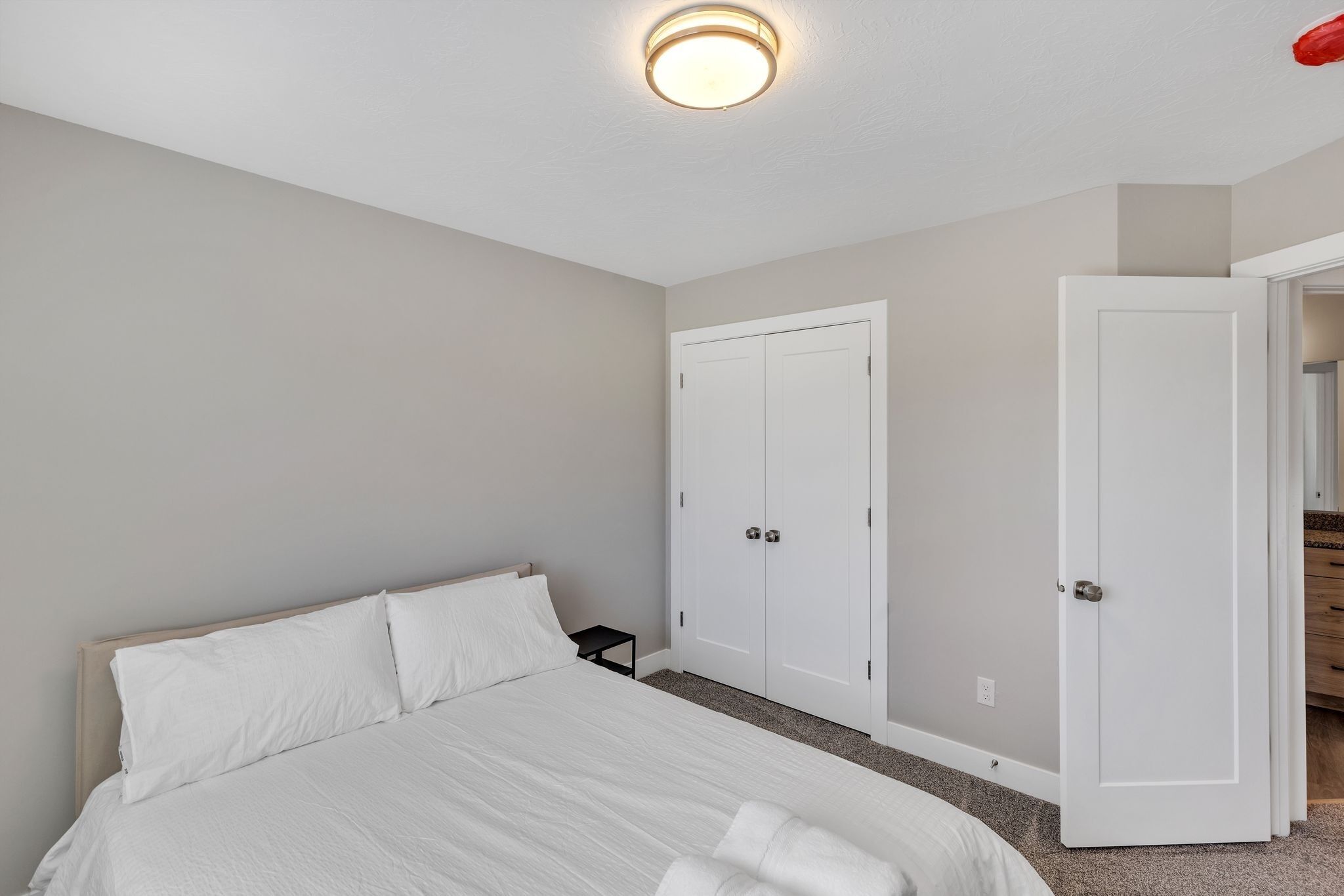 A bedroom with a bed, two white doors, a nightstand, and a ceiling light.