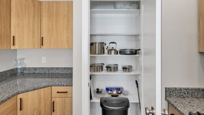A kitchen with wooden cabinets, granite countertops, and stainless steel cookware on shelves.