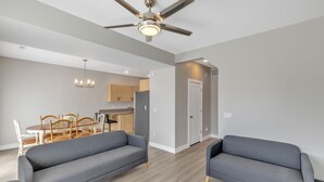 A modern living room with grey sofas, a dining area with wooden chairs, and a kitchen in the background.