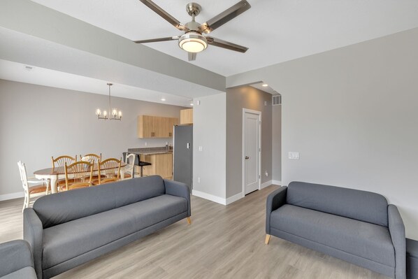 A modern living room with grey sofas, a dining area with wooden chairs, and a kitchen in the background. - The Ideal Gateway by RedAwning (Cedar City)