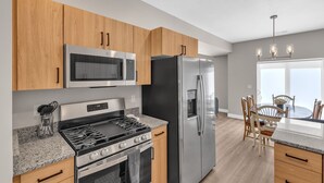 A modern kitchen with stainless steel appliances, wooden cabinets, granite countertops, and a dining area with a table and chairs.