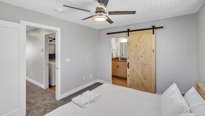 A bedroom with a bed, a ceiling fan, a wooden wardrobe, and a bathroom visible through an open door.