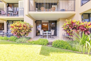 A two-story building with a balcony, outdoor seating area, and lush landscaping. - Kamaole Sands 6-107 1 Bedroom Condo (Kihei)