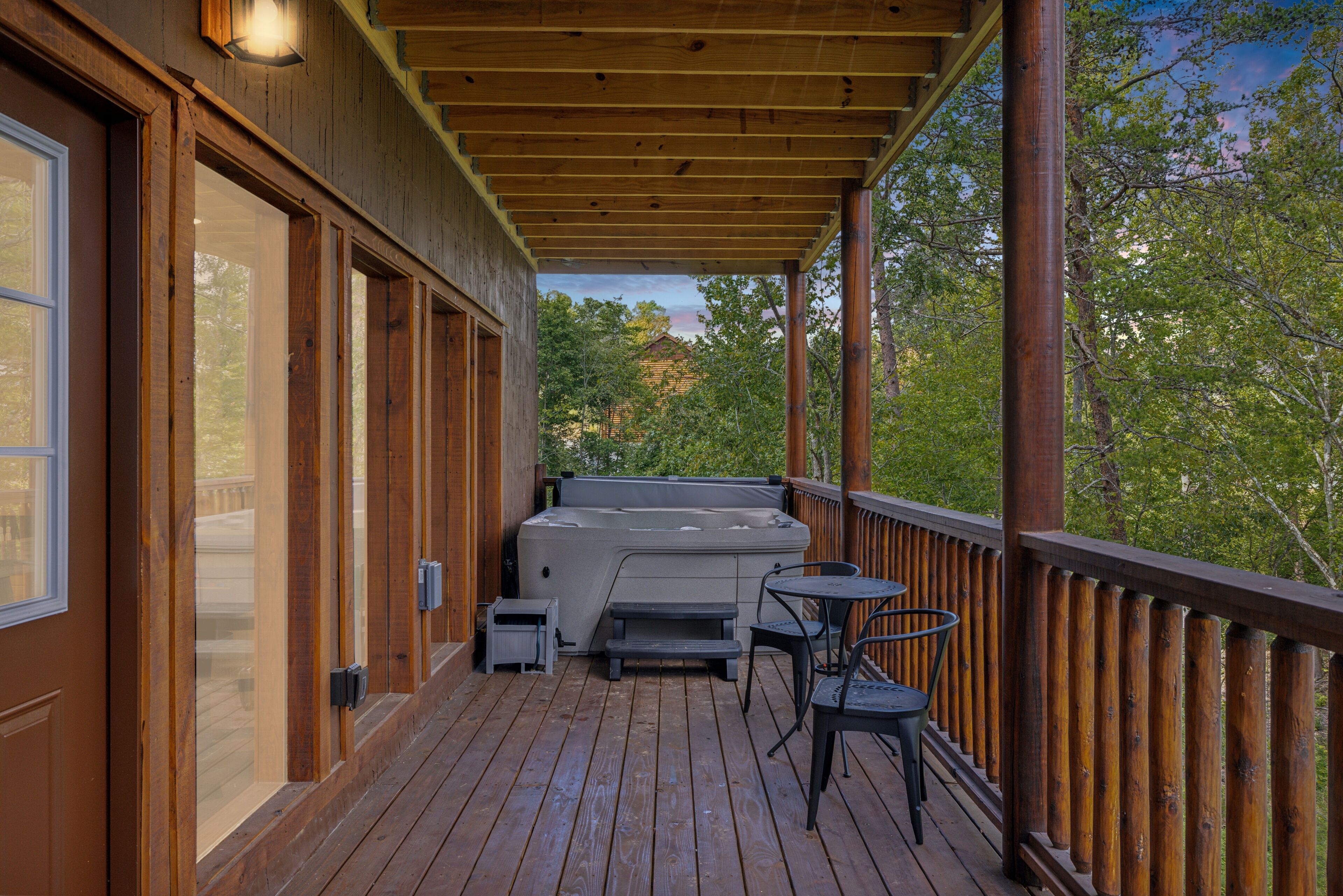 A wooden deck with a hot tub, outdoor seating, and a view of trees.