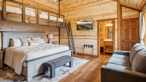 Un dormitorio de cabaña de madera con cama, banco y vistas a las montañas a través de una ventana.