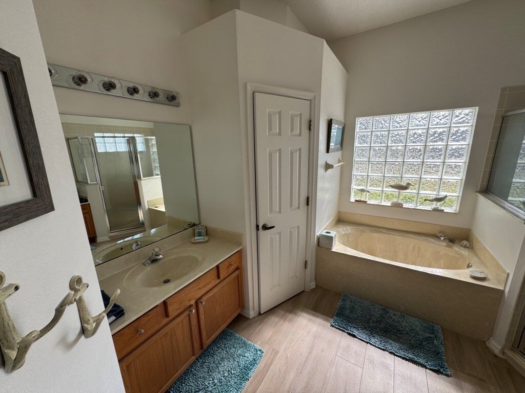 A bathroom with two sinks, a large mirror, a door, a window with a view, and a bathtub.