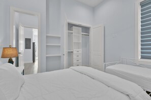 A bedroom with a bed, a bedside table with a lamp, a wardrobe, and a window with blinds. - Cielito Lindo - Private Home With Hot Tub 3 Bedroom Home by RedAwning (South Padre Island)