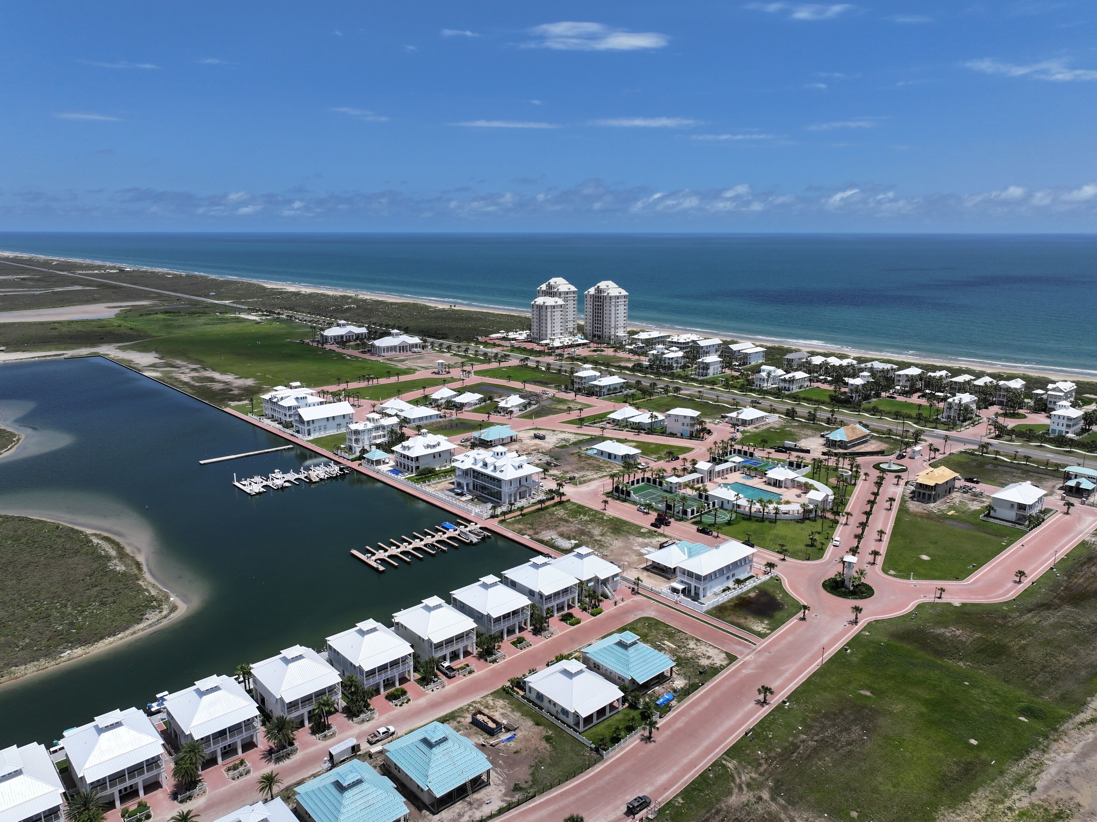 Vista aérea de un complejo turístico costero con varios edificios, un puerto deportivo y una playa.