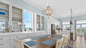Une cuisine moderne avec des meubles blancs, une table à manger en bois agrémentée de sets de table bleus et un lustre.