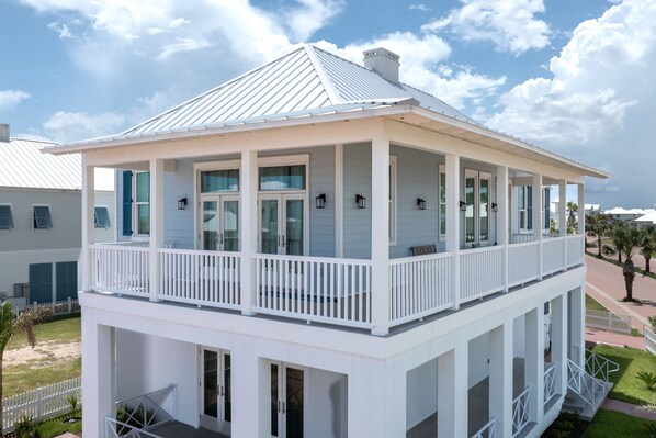 A two-story white building with a balcony, large windows, and a covered porch area. - Seaside Rendezvous - Private Home Across From Community Park 4 Bedroom Home by RedAwning (South Padre Island)