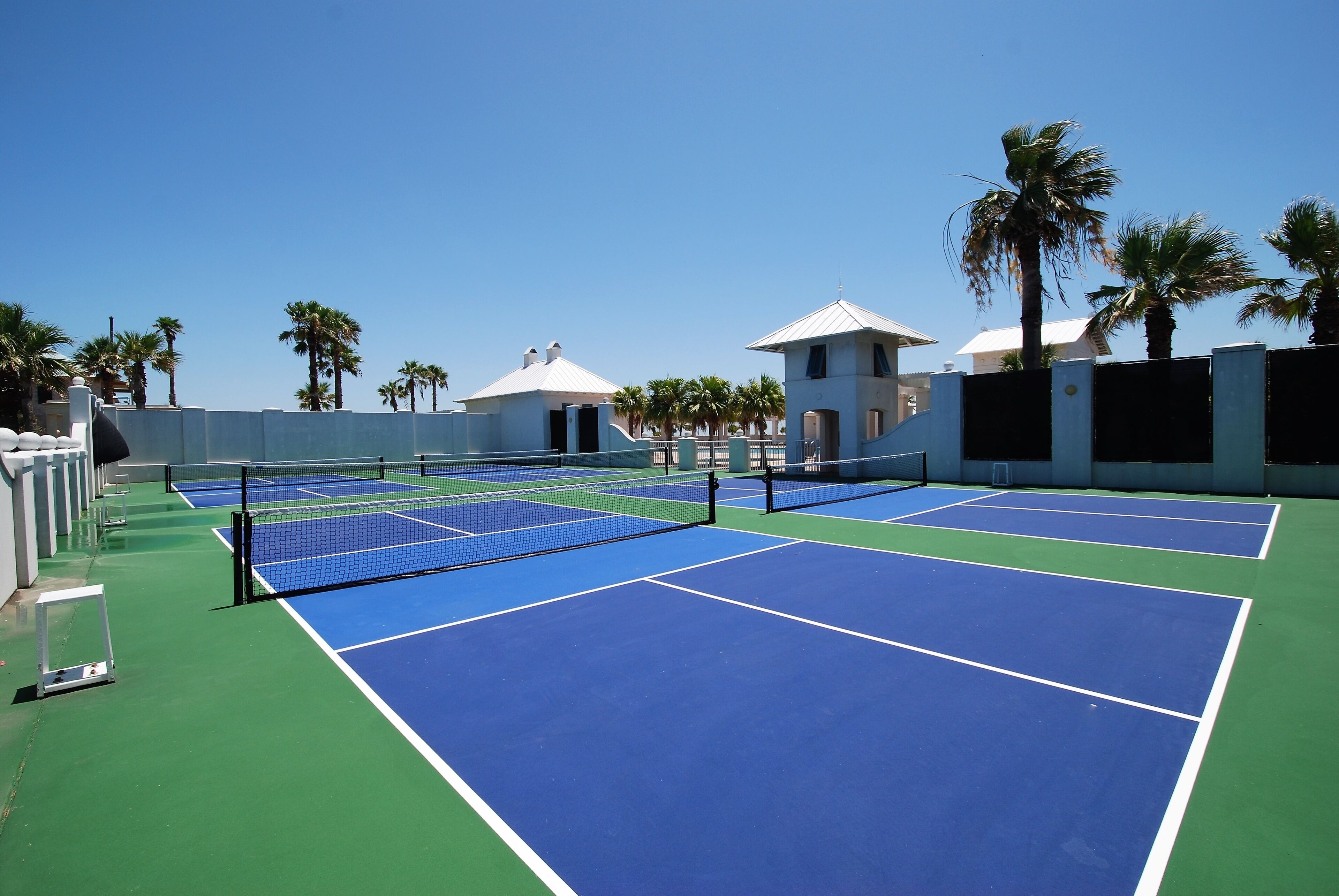 Ein Tennisplatz mit mehreren Spielplätzen, Palmen und einem Gebäude mit weißem Dach.