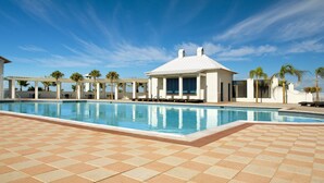 Area piscina con cielo azzurro, un edificio bianco con colonne e palme.