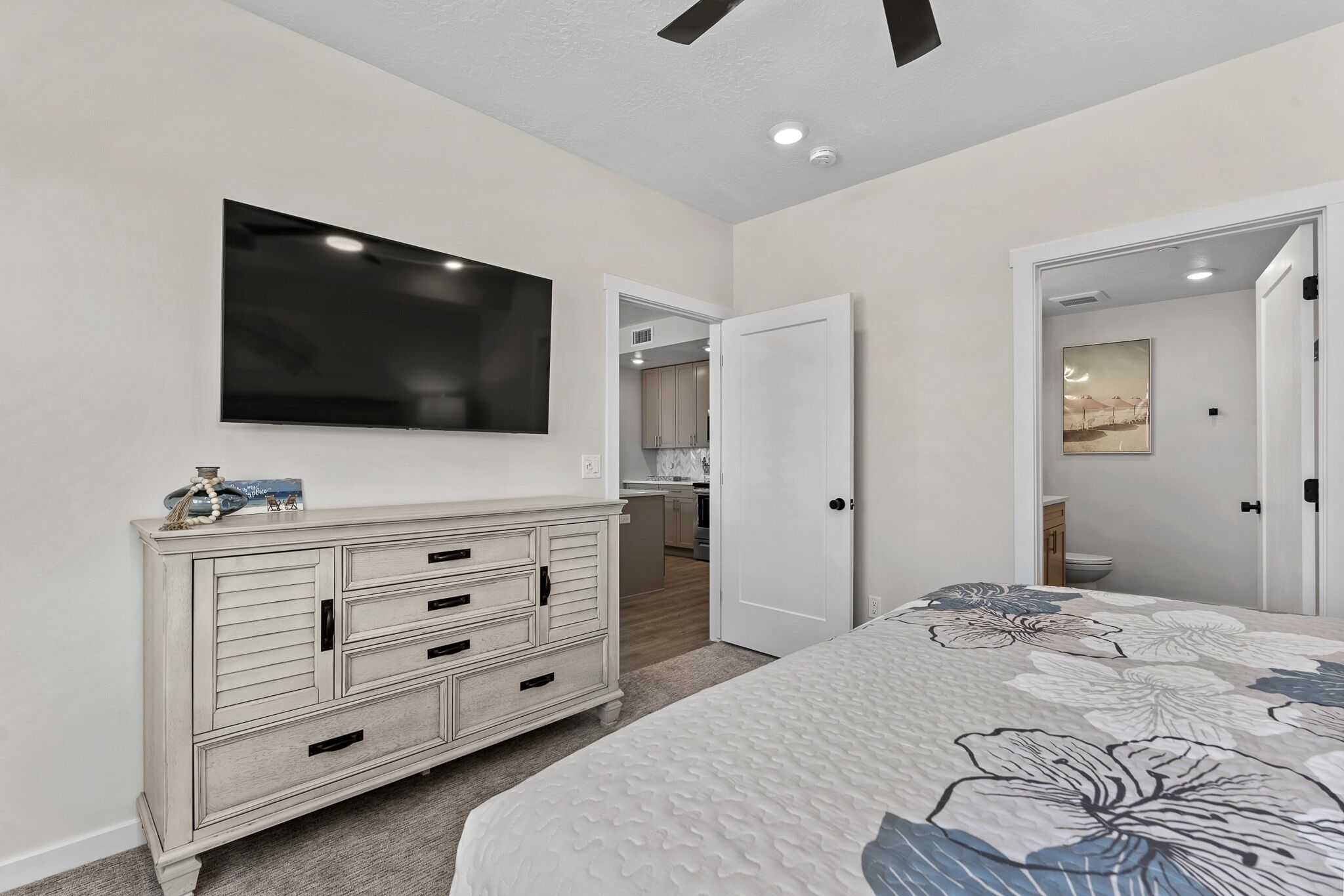 A bedroom with a bed, a dresser, a TV, and a door leading to a bathroom.