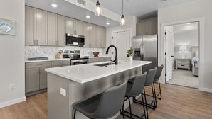 Una cocina moderna con una isla central, armarios grises, electrodomésticos de acero inoxidable e iluminación colgante.