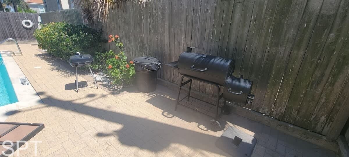 A backyard with a pool, a grill, and a trash can.