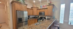 A kitchen with wooden cabinets, stainless steel appliances, granite countertops, and a window with decorative glass. - Island Time #4 2 Bedroom Condo by RedAwning (South Padre Island)