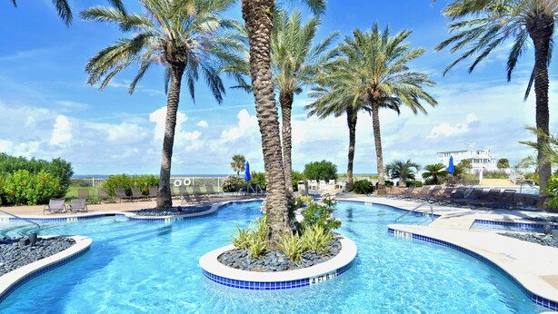 Ein Swimmingpool mit einer kreisförmigen Insel, Palmen und Liegestühlen.