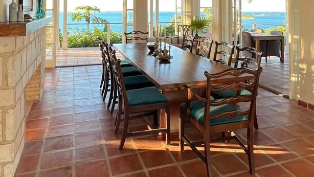 A spacious dining area with a long table and chairs, large windows offering a view of the ocean, and a high ceiling with exposed beams. - Big Hill - a luxurious haven that will not disappoint, View Sunrise, Dock (Elbow Cay)