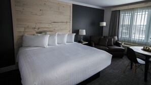A hotel room with a large bed, a desk, a chair, a sofa, and a window with curtains. - Hôtel Napoléon (Gatineau)