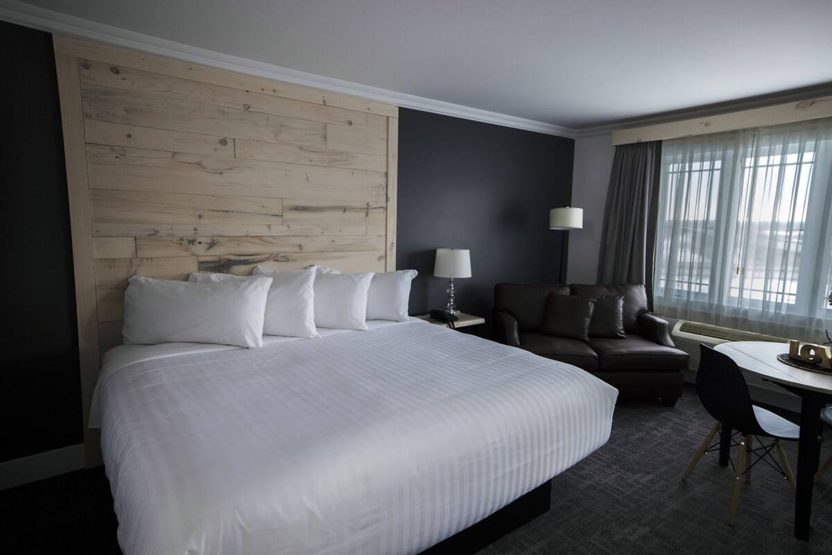 Une chambre d’hôtel avec un grand lit, un bureau, une chaise, un canapé et une fenêtre avec des rideaux.