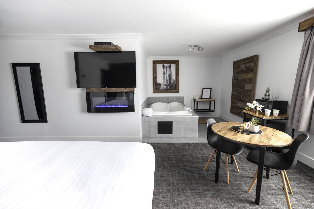 Une chambre d’hôtel avec un lit, un téléviseur fixé au mur, une cheminée, une petite table avec des chaises et un grand miroir.