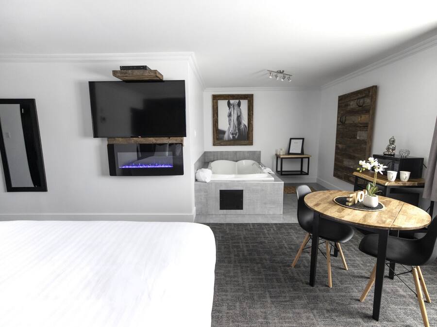 Quarto de hotel com cama, televisão na parede, lareira, pequena mesa com cadeiras e um espelho grande.