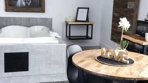 A modern room with a gray carpet, a round wooden table with "LOVE" letters, black chairs, a gray sofa, a framed horse painting, and a stone wall. - Hôtel Napoléon (Gatineau)