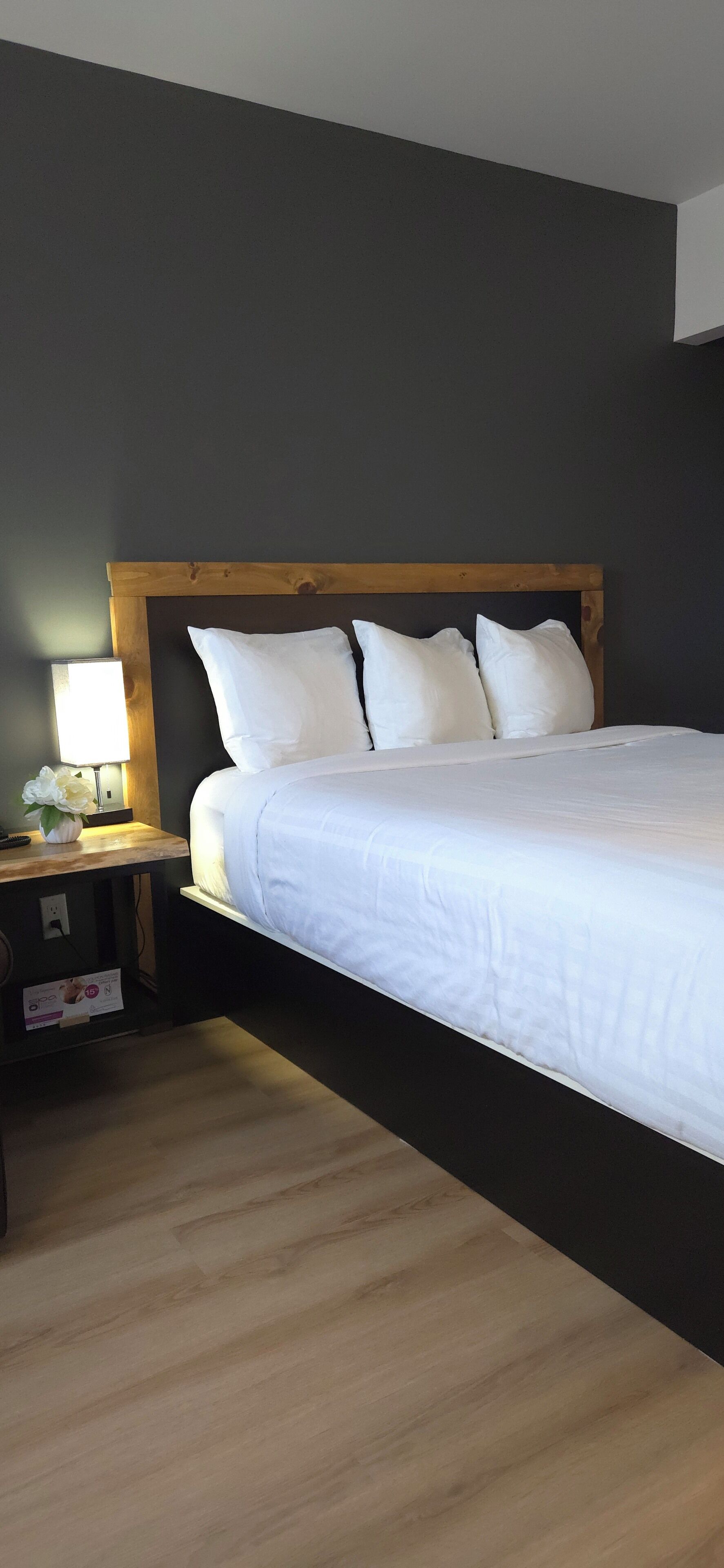 A bedroom with a wooden headboard, white bedding, a bedside table with a lamp, and a nightstand.