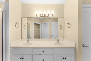 A bathroom with a double sink vanity, a large mirror, and a light fixture above the mirror. - Beachfront resort condo w/ Gulf balcony views (Panama City Beach)
