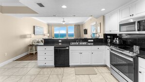 A modern kitchen with white cabinets, a black countertop, and stainless steel appliances. - Beachfront resort condo w/ beach access (Panama City Beach)