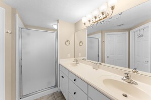 A bathroom with a large mirror, a sink, a shower, and a vanity with drawers.