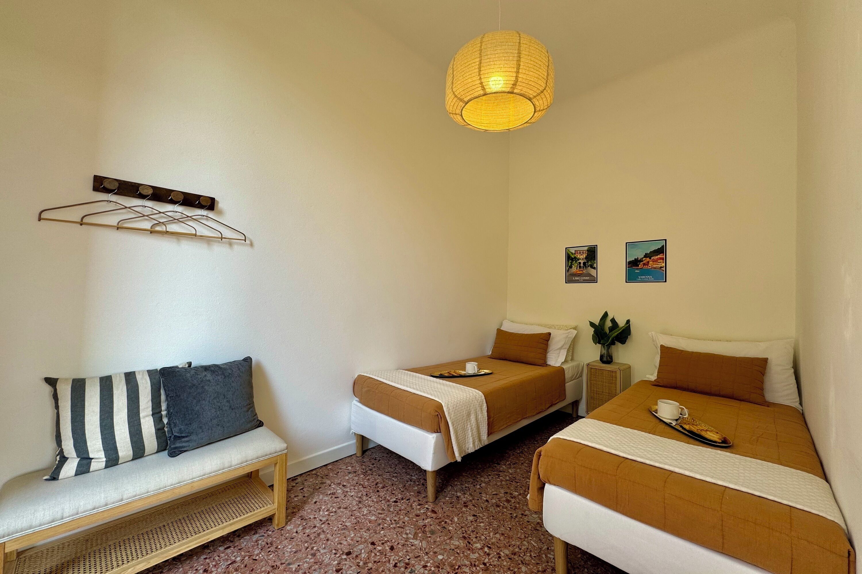 Ein Zimmer mit zwei Einzelbetten, einer Sitzbank, einer Hängeleuchte und einem kleinen Tisch mit einer Pflanze.