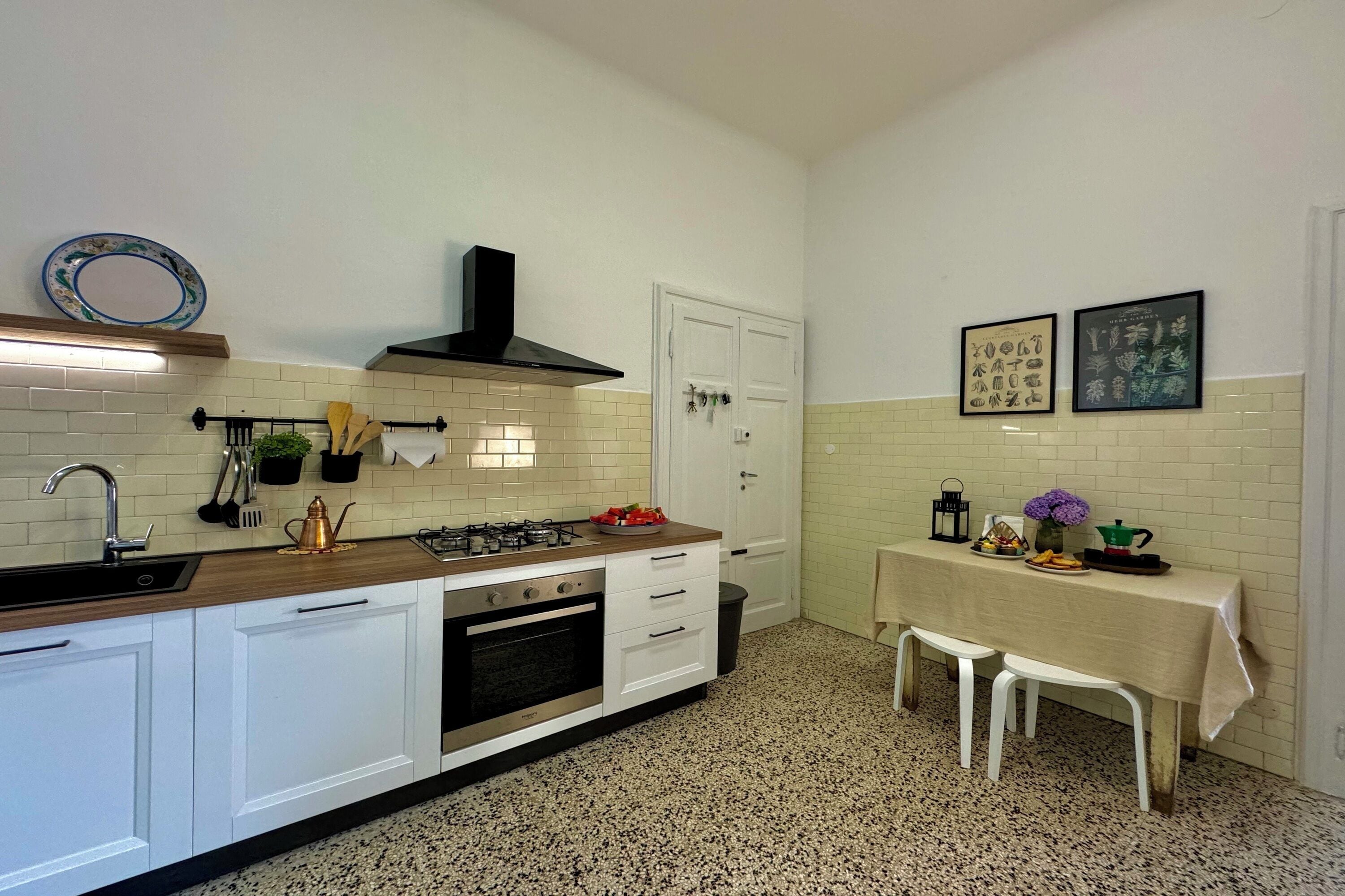 A kitchen with white cabinets, a stove, and a sink. There is a table with a tablecloth and chairs.