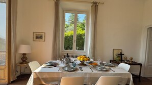 Una sala da pranzo con tavolo apparecchiato per quattro persone, una finestra con tende, una lampada e un termosifone.