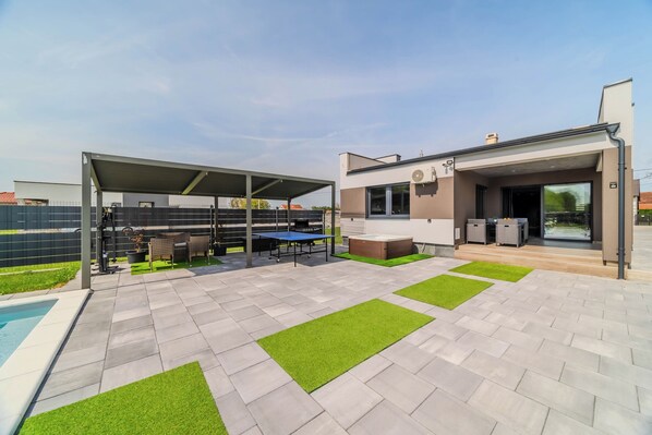 A modern outdoor patio with a pool, covered seating area, and a well-maintained lawn. - Villa Joy With Pool and Hot Tub (Sracinec)