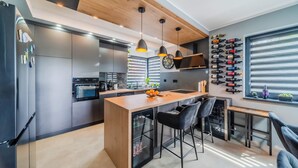 Una cocina moderna con una isla central, taburetes de bar, un botellero y un ventanal grande.
