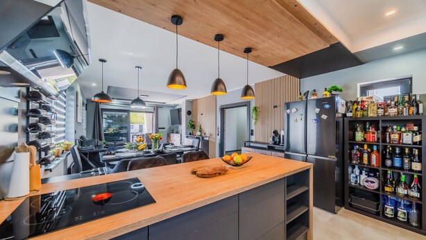 Una cocina moderna con una isla central, iluminación colgante y un refrigerador para vino empotrado.