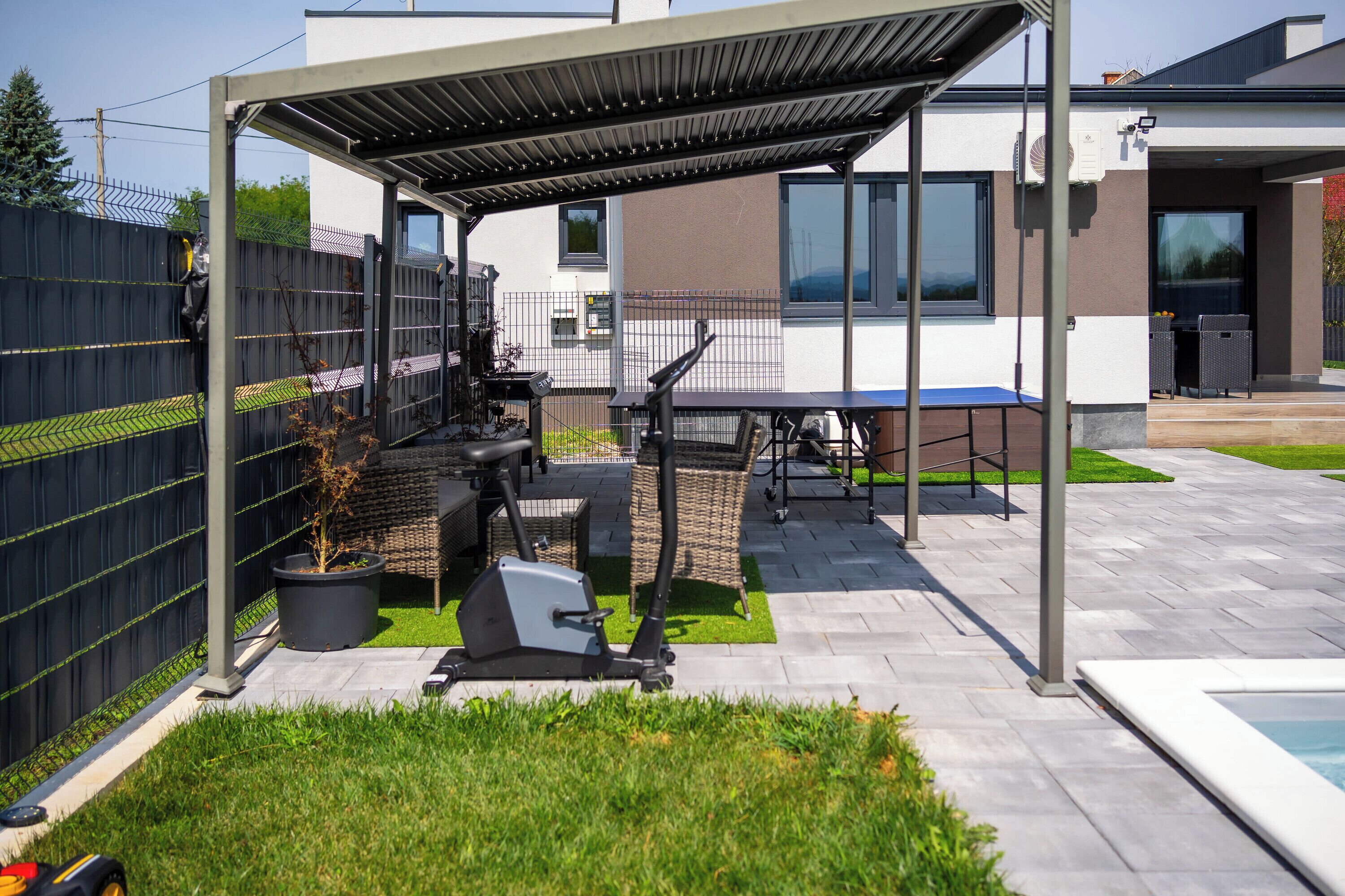 A covered outdoor area with exercise equipment, a table, and a pool.