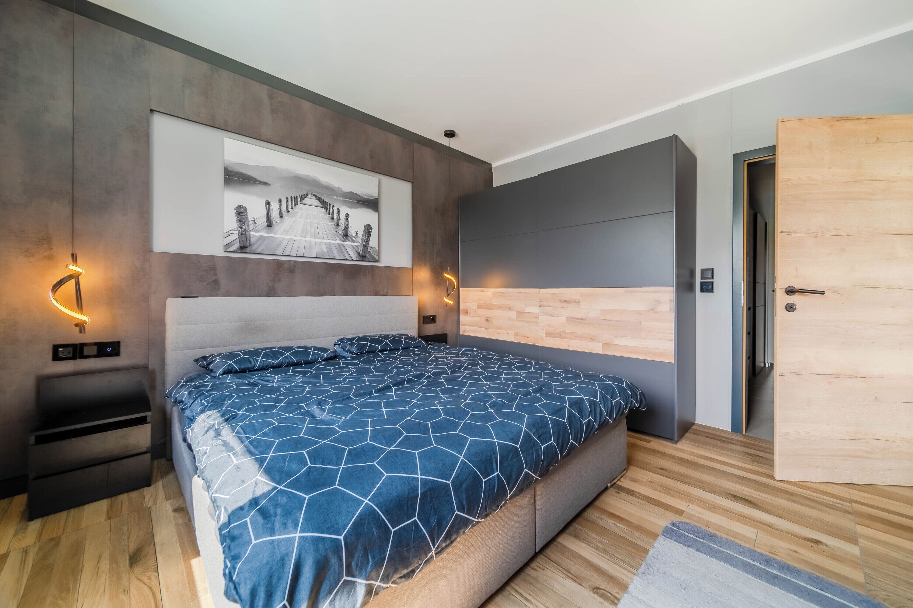 Un dormitorio moderno con una cama grande, piso de madera, una puerta de madera y una obra de arte colgada en la pared.