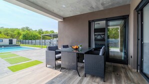 Un patio moderno al aire libre con una mesa de comedor, sillas y vista a una piscina.