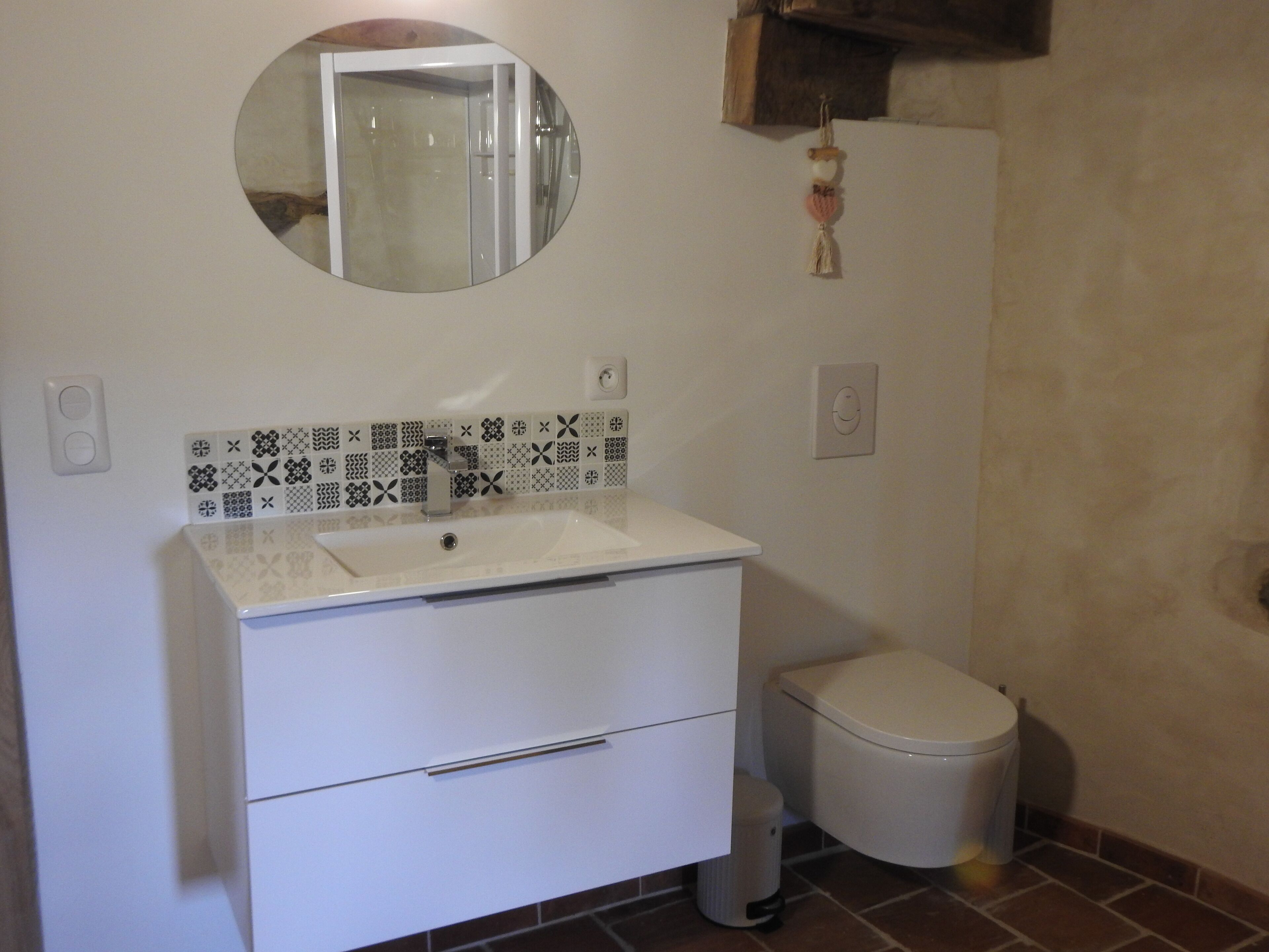 Une salle de bain avec un meuble-lavabo blanc, un évier, un miroir, des toilettes et des carreaux décoratifs sur le mur.