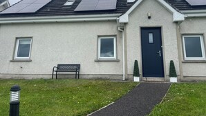A house with a black door, two windows, a bench, and solar panels on the roof.