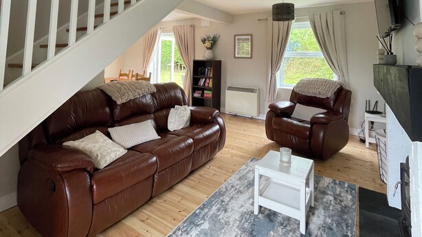 A spacious living room with a high ceiling, a staircase, leather sofas, a coffee table, and a fireplace.