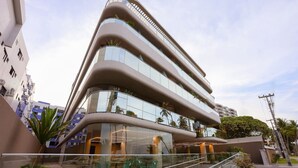 A modern multi-story building with a curved facade, large windows, and a glass staircase leading to an outdoor seating area. - Setai Yacht Luxxor - By Almare Flats (João Pessoa)