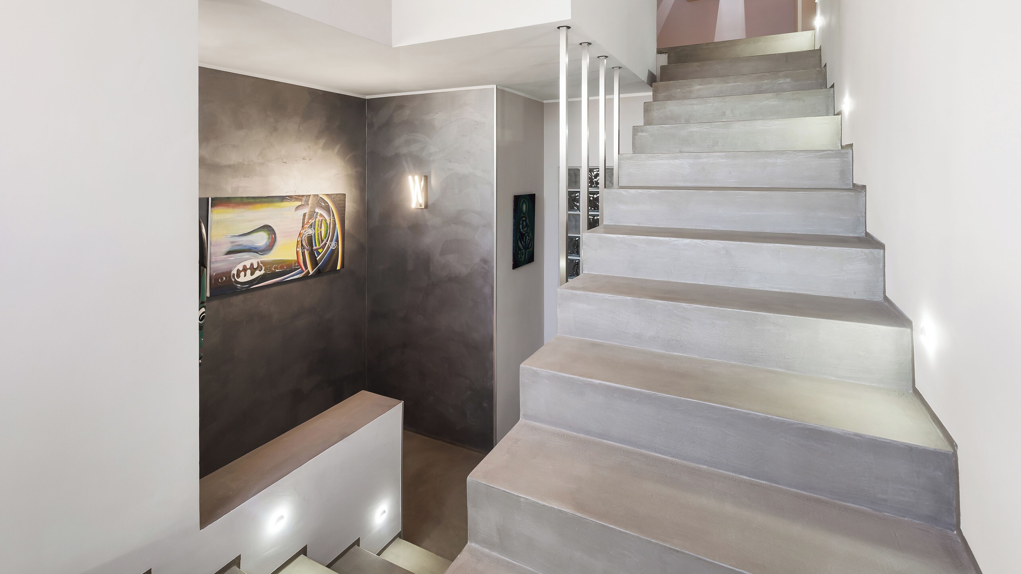 A modern staircase with a minimalist design, a dark wall with a painting, and a light-colored floor.