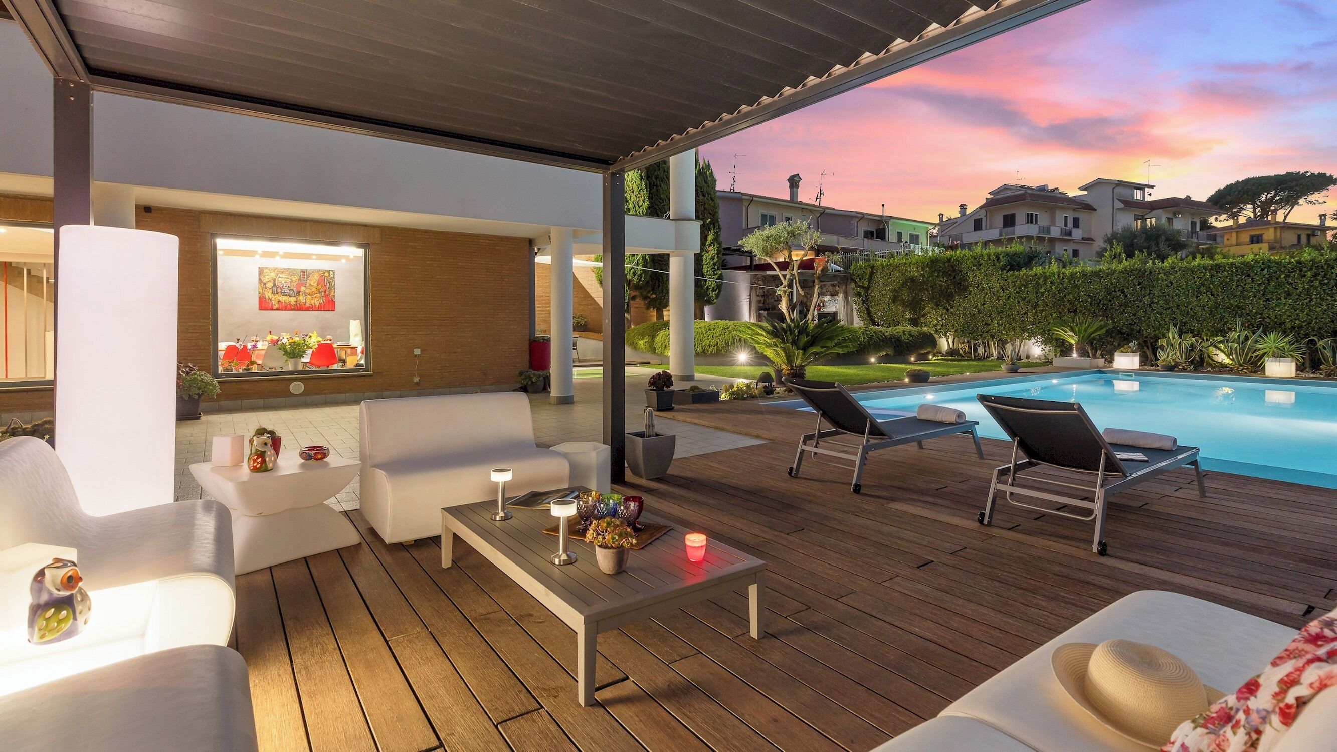 A covered outdoor area with a pool, lounge chairs, and a seating area with a table and cushions.