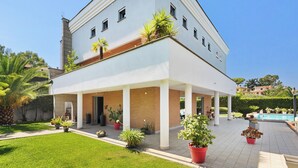 A modern two-story building with a covered patio area, a swimming pool, and various potted plants. - Villa Tiberio 6+2, Emma Villas (Genzano di Roma)