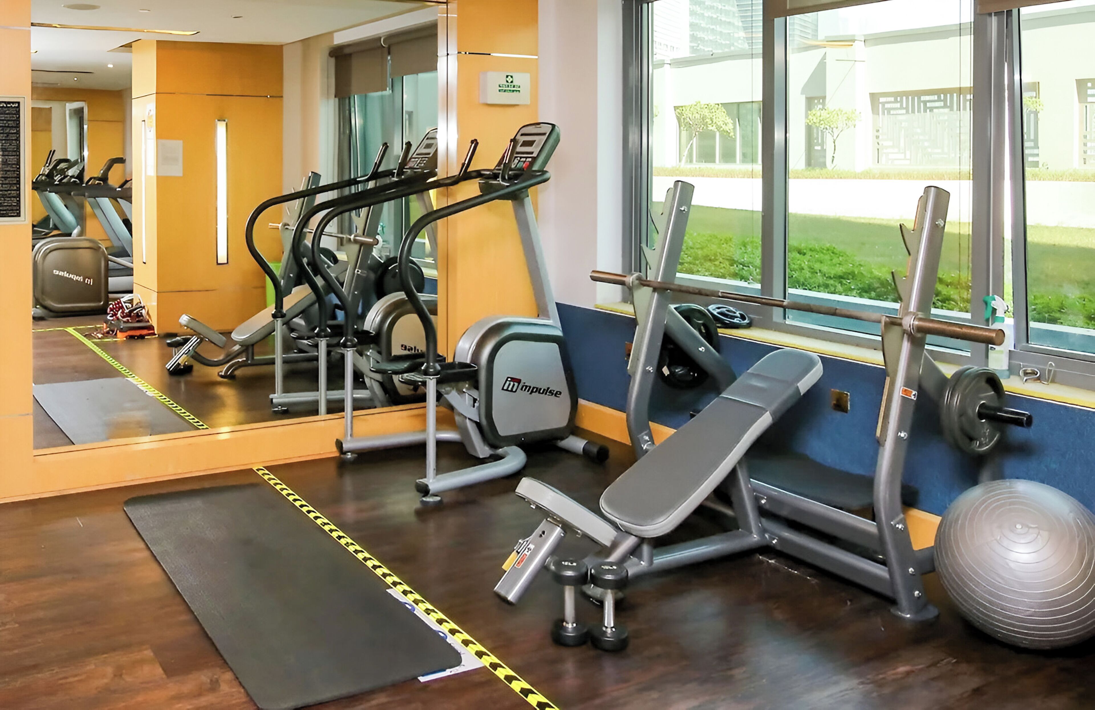 A gym with cardio machines, a bench press, and a mirror.